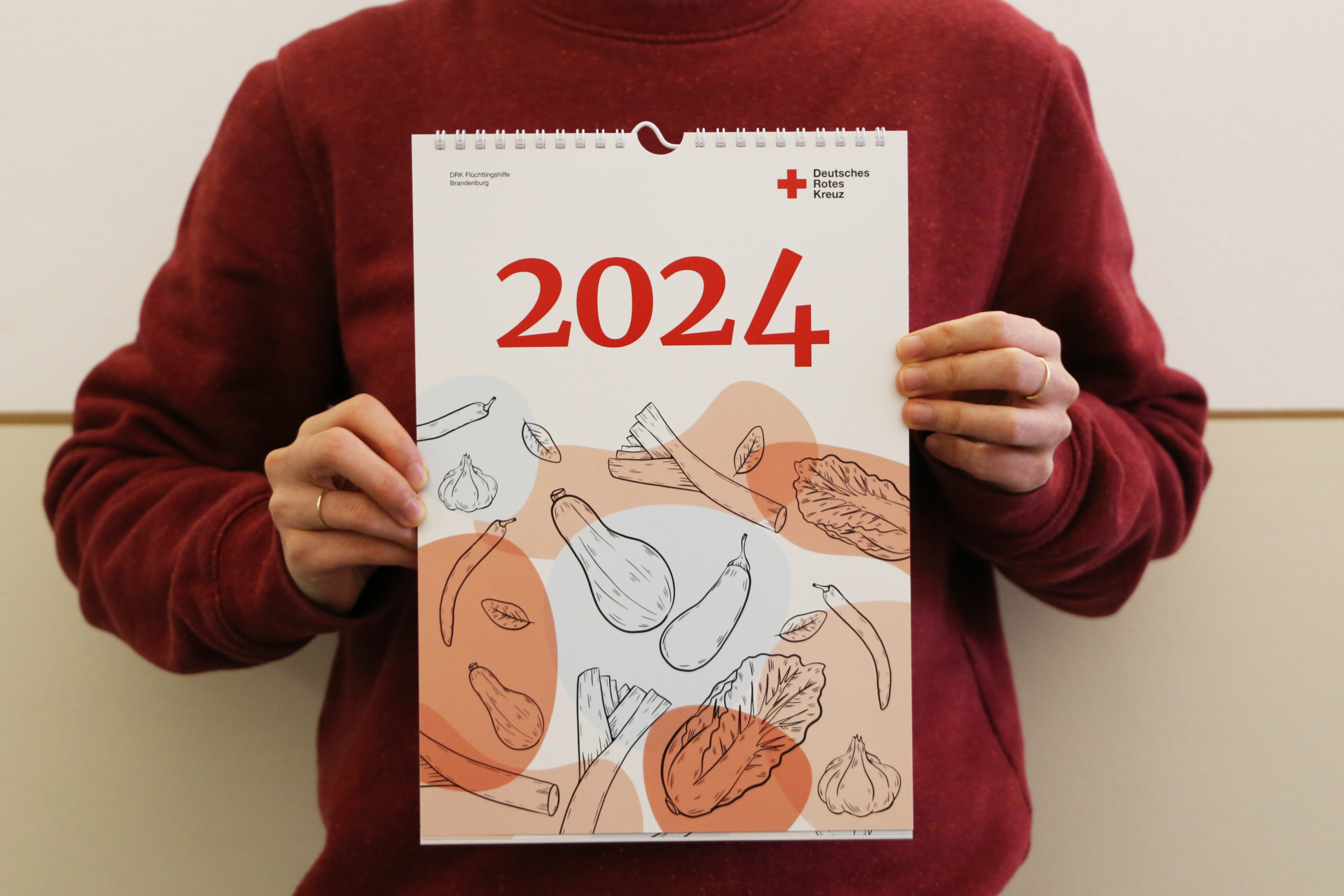 Eine Person hält einen Wandkalender für das Jahr 2024 in die Kamera